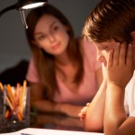 Teenage Sister Helping Stressed Younger Brother With Studies At Desk In Bedroom In Evening