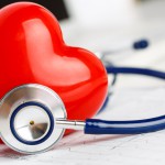 Medical stethoscope and red toy heart lying on cardiogram chart